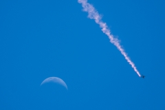 Sky diver streams past a crescent moon.